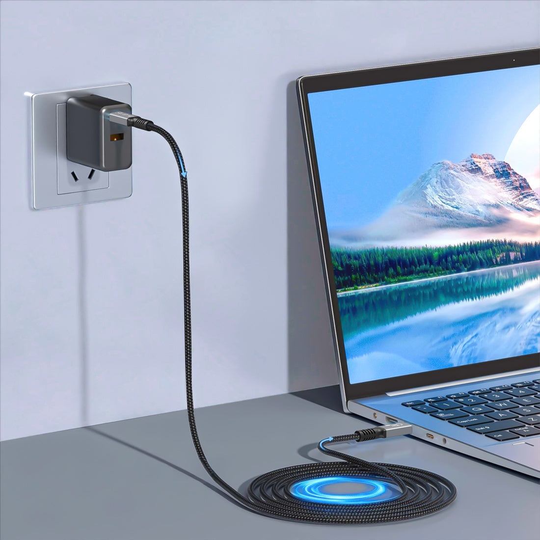 Laptop connected to a power adapter with a mountainous landscape displayed on the screen.
